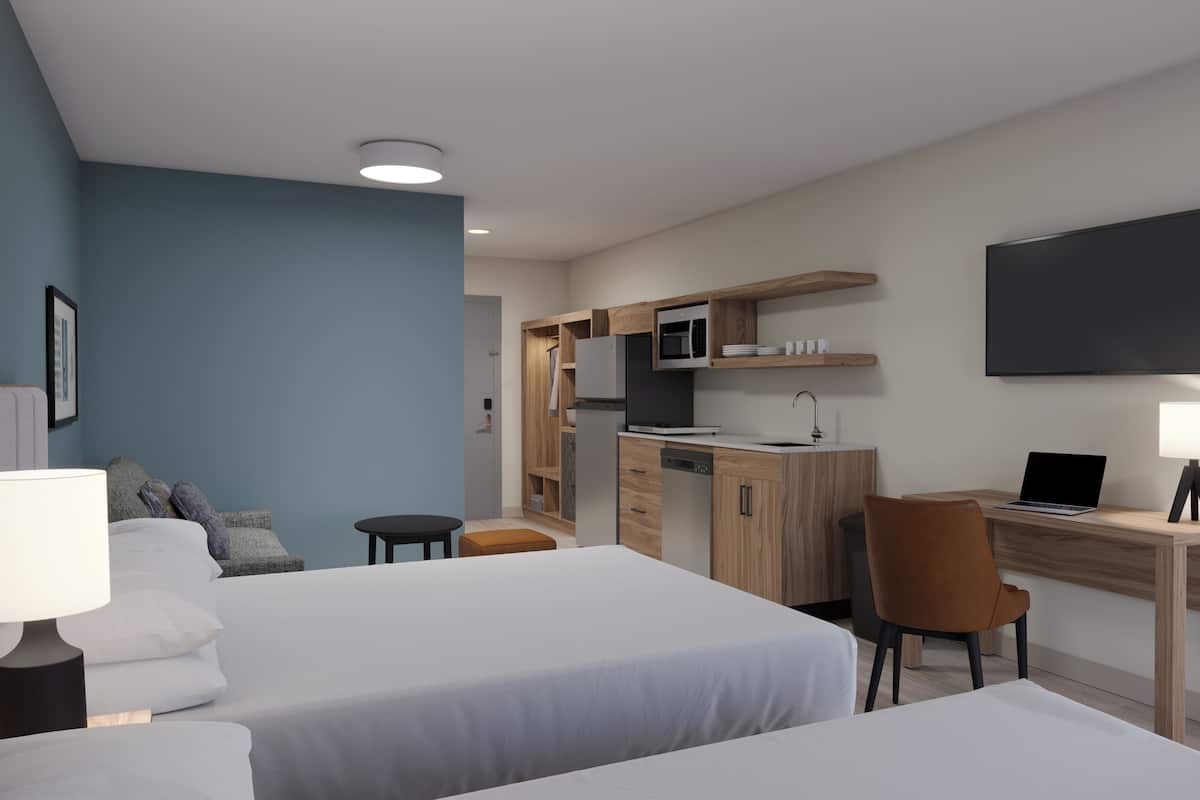 Hotellihuone, jossa on kaksi sänkyä, työpöytä, tuoli, televisio ja lamppu.