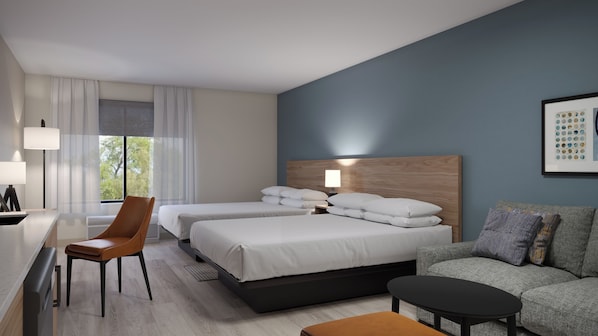 A hotel room with two beds, a desk, a chair, a sofa, and a coffee table.