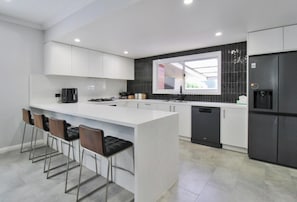 Una cocina moderna con armarios blancos, una isla central con taburetes, un refrigerador negro y una ventana con vistas.