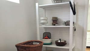 Een compacte keuken met een vaatwasser, een kleine koelkast en een wit wandrek met keukengerei.