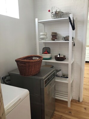 Eine kompakte Küche mit Geschirrspüler, kleinem Kühlschrank und einem weißen Regal mit Geschirr.