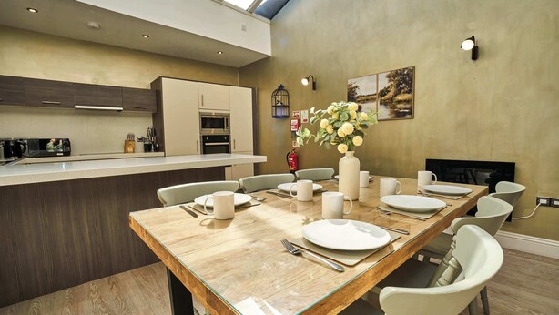 A modern kitchen with a dining area, including a wooden table set for four, a vase of flowers, and a fireplace. - York City Centre | Shambles & Minster Walk (York)