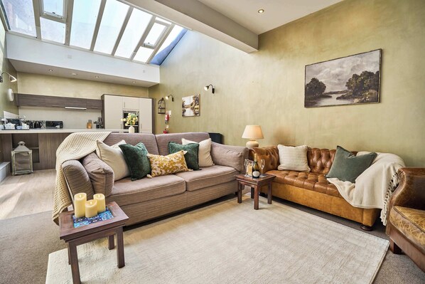 A spacious living area with a high ceiling, a skylight, a sofa set, a coffee table, and a painting on the wall.