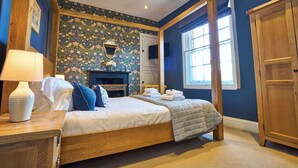 A bedroom with a four-poster bed, a fireplace, a wooden wardrobe, and a large window. - York City Centre | Shambles & Minster Walk (York)