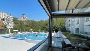 A balcony with a view of a swimming pool, a dining area, and surrounding buildings. - Status M Apartments 176 (Becici)