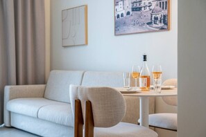 A modern living room with a sofa, a dining table with glasses and a bottle, and a framed picture on the wall.