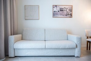 A light-colored sofa in a room with a plain wall, a framed picture, and a chair.