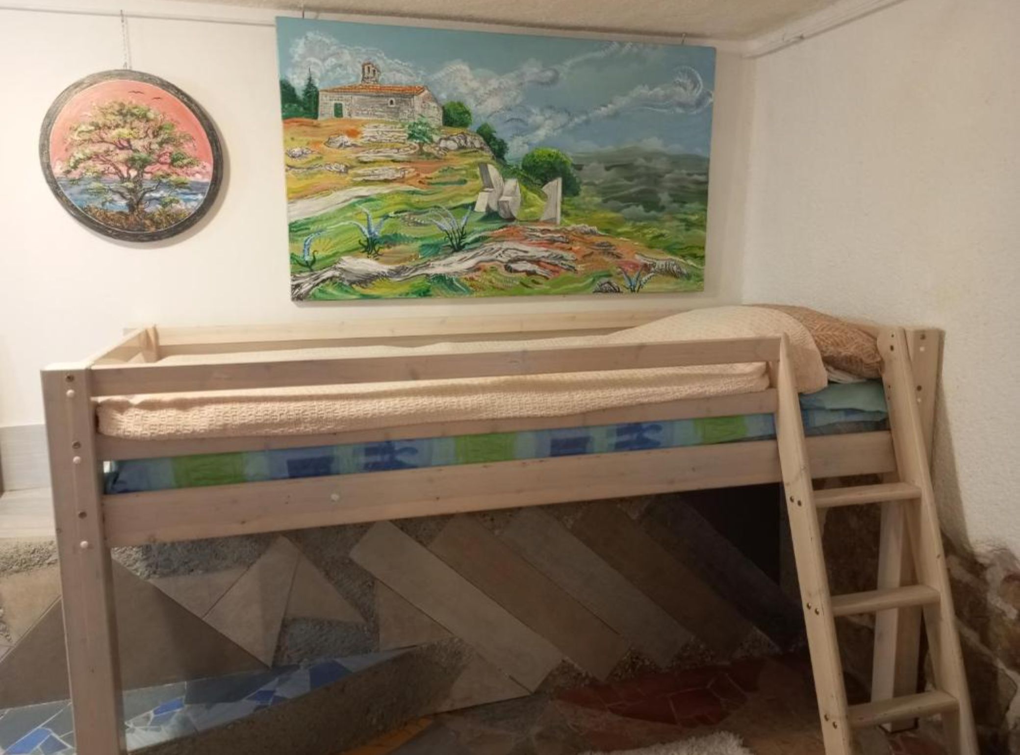 A bunk bed with a ladder, a painting of a landscape, and a framed picture on the wall.