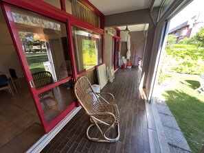 Ein Zimmer mit einem Korbstuhl, einem Fenster mit rotem Rahmen und Blick auf einen Garten.