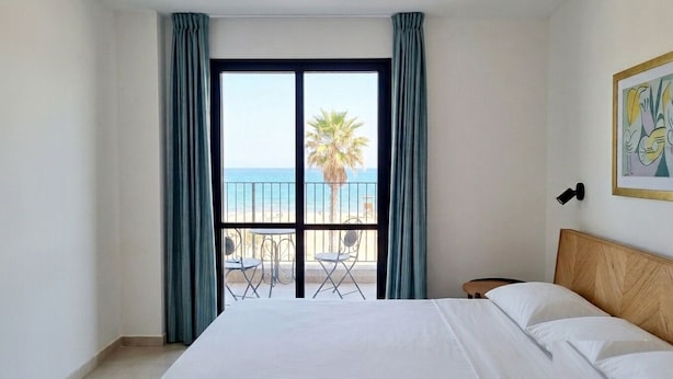 A hotel room with a bed, a view of the beach, and a balcony with chairs. - Urban Penthouse Loft W Jacuzzi (Haifa)