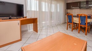 A modern kitchen with a flat-screen TV, wooden furniture, and a dining area with chairs and a table. - Apartments Aurel Suites (Rogoznica)