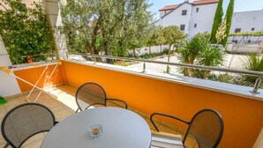 A balcony with a round table and four chairs, a small glass on the table, and a view of buildings and trees. - Apartments Aurel Suites (Rogoznica)