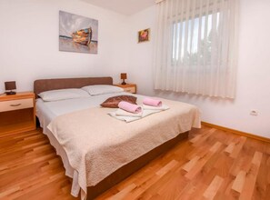 Ein Schlafzimmer mit einem Bett, Nachttischen, einem Fenster mit durchsichtigen Vorhängen und einem Bild an der Wand.