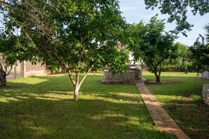 A grassy area with a brick pathway, trees, and a stone structure.