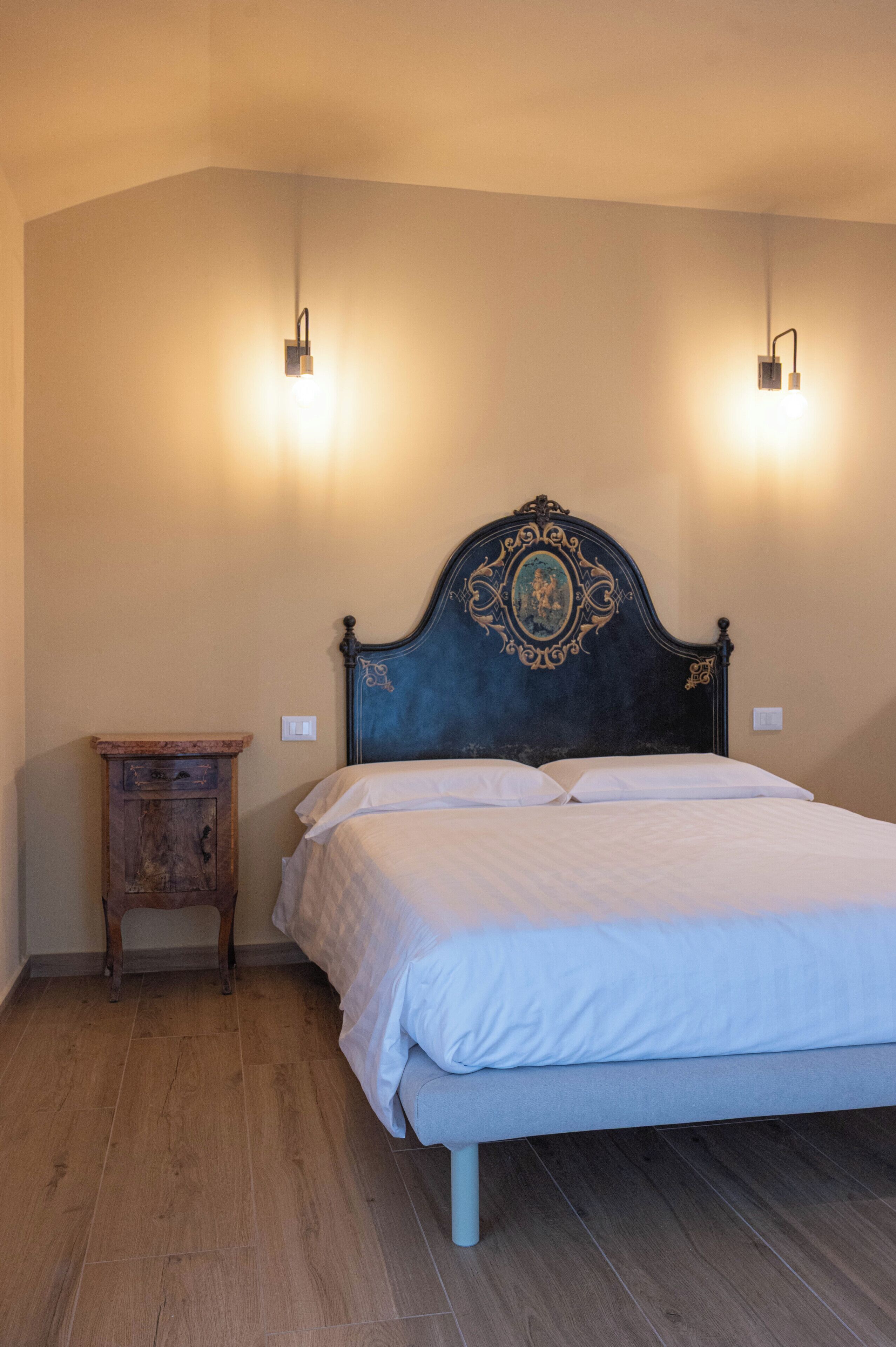 Un dormitorio con cama, mesita de noche de madera y dos lámparas fijadas a la pared.