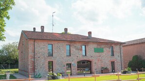 A brick building with a tiled roof, a sign reading 'BUTT,' and a paved area with benches. - Relais Monastero (Podenzano)