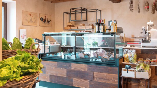A rustic interior with exposed wooden beams, a glass display case with food items, wicker baskets, and a tiled floor. - Relais Monastero (Podenzano)