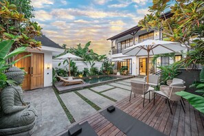Una casa moderna con piscina, mobiliario exterior y abundante vegetación.