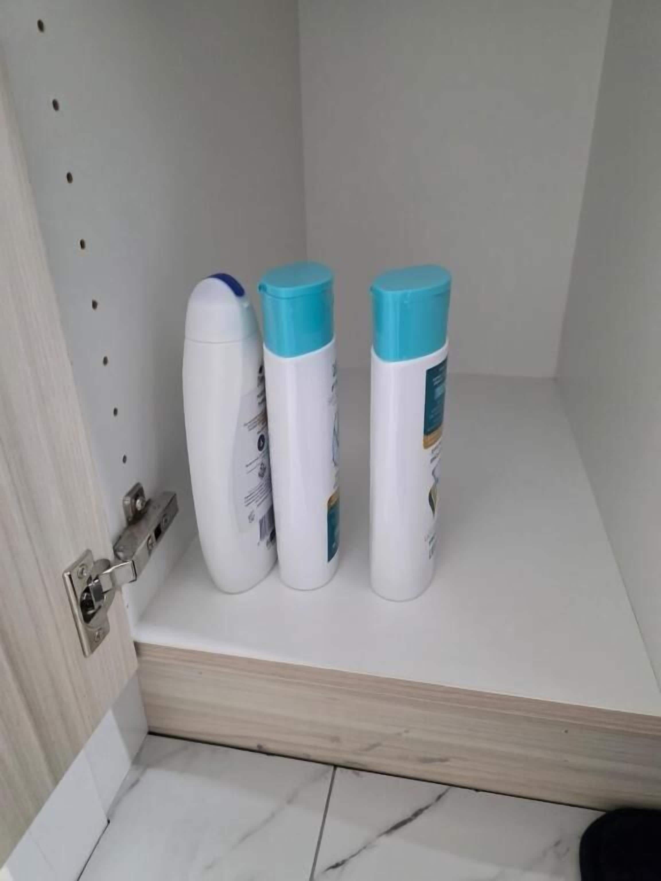 A bathroom with a white sink, a mirror, and three toiletry bottles on a shelf.
