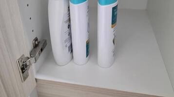 A bathroom with a white sink, a mirror, and three toiletry bottles on a shelf.