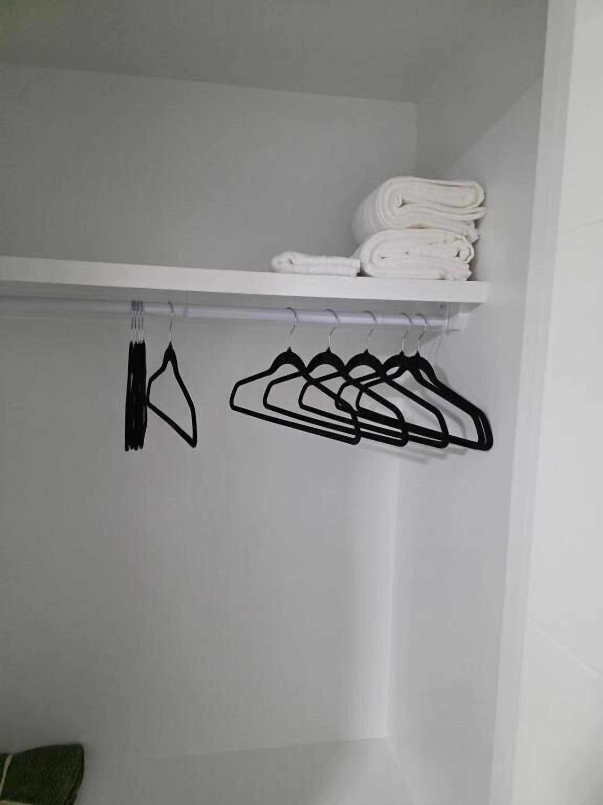 A closet with a white shelf holding folded towels and a row of black hangers.
