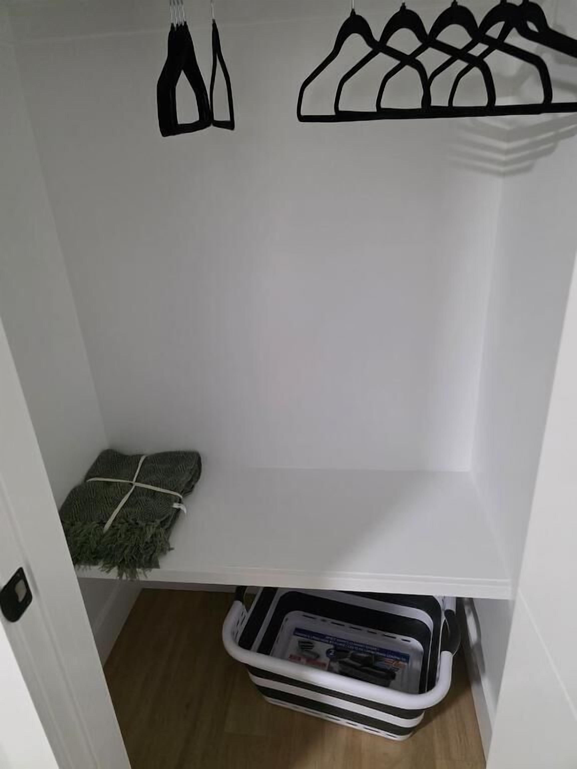 A small, white closet with a hanging rack and a storage bin.