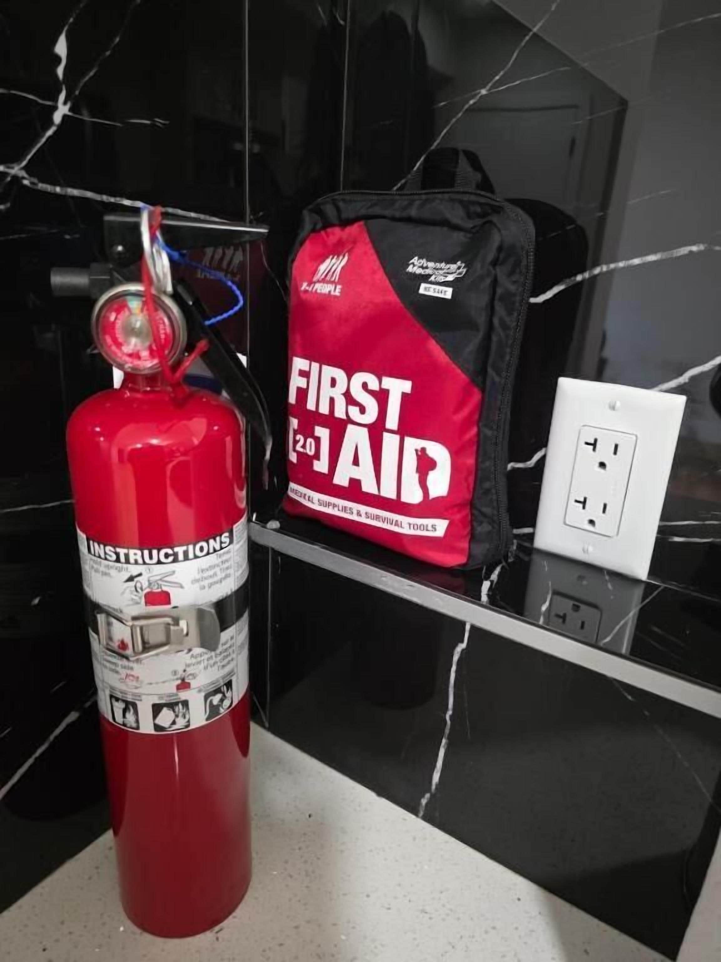 Un estintore rosso e una borsa nera con la scritta 'FIRST AID' su un piano di marmo nero.