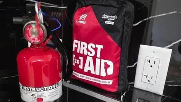 Un estintore rosso e una borsa nera con la scritta 'FIRST AID' su un piano di marmo nero.