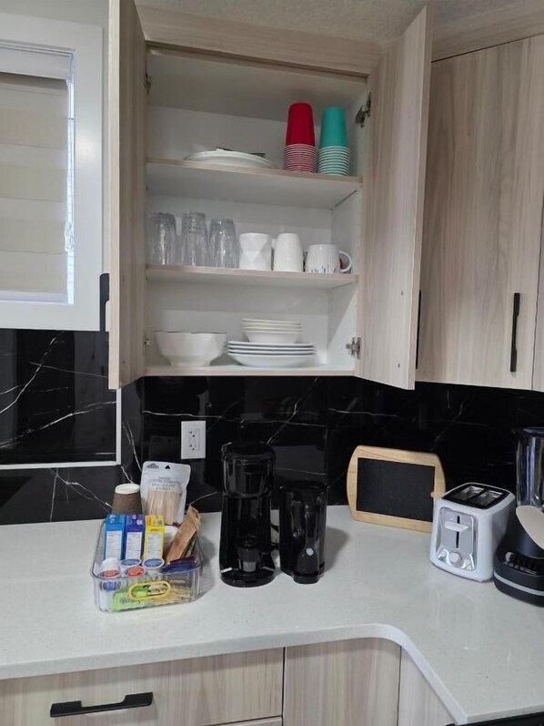 A kitchen with a white countertop, a coffee maker, a toaster, and a cabinet with dishes and cups.