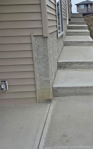 A residential building with beige siding, a stone foundation, and concrete steps leading to the entrance. - Cozy Irvine Creek Walk-out Suite 10 Mins to YEG (Leduc County)