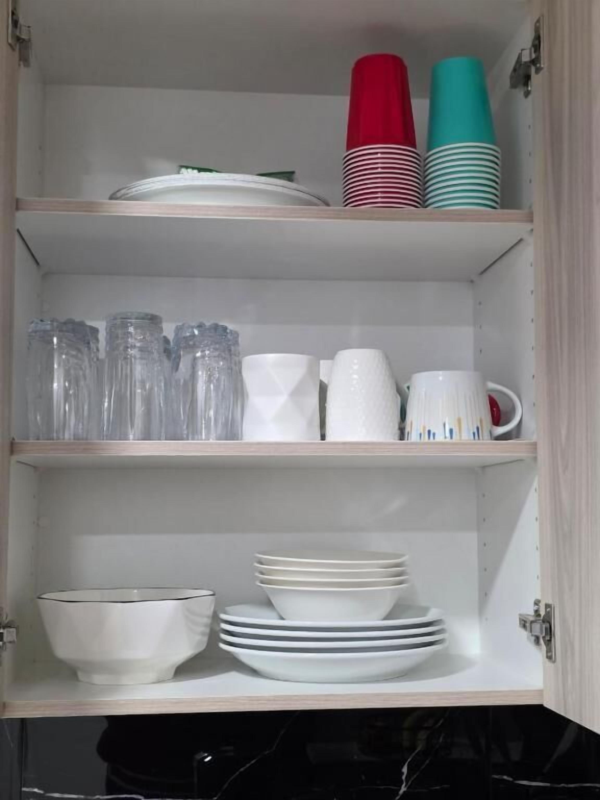 A kitchen cabinet with shelves containing glassware, plates, and cups.