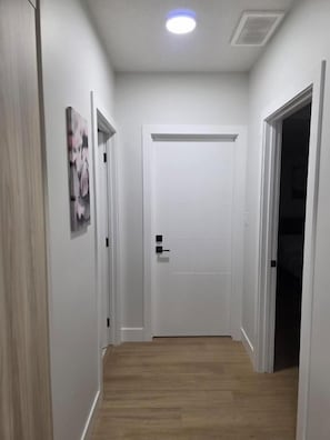 A hallway with a wooden floor, white walls, and a closed door at the end. - Cozy Irvine Creek Walk-out Suite 10 Mins to YEG (Leduc County)