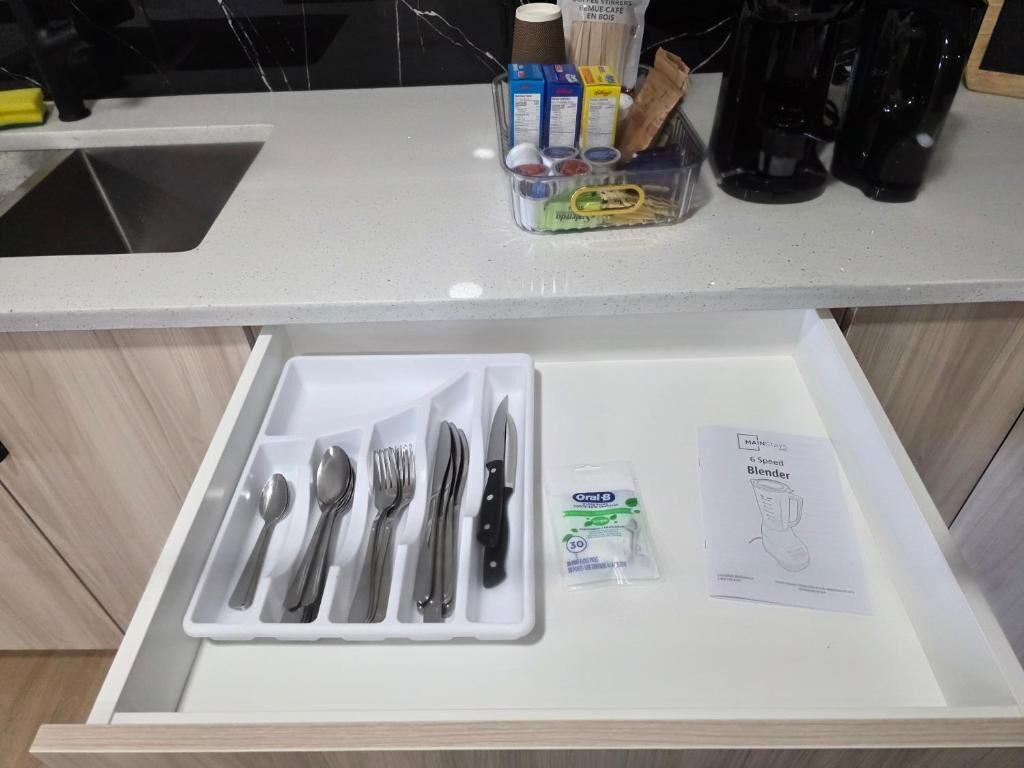 A kitchen counter with a drawer containing utensils and a packet of Oral-B toothpaste.