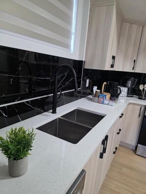 A modern kitchen with a black marble backsplash, a white countertop, and a black faucet. There is a potted plant on the counter and a coffee maker on the right.