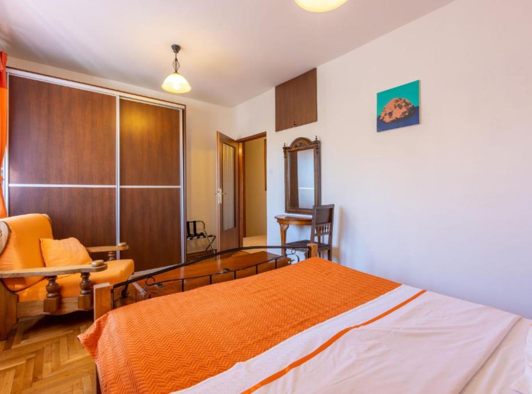 A hotel room with a bed, a chair, a desk, a mirror, and a wardrobe.