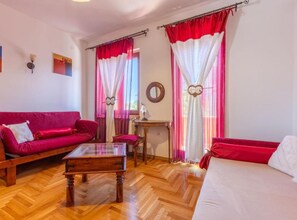 Una habitación con un sofá rojo, una mesa de centro de madera, un sofá blanco y una mesita con una lámpara.