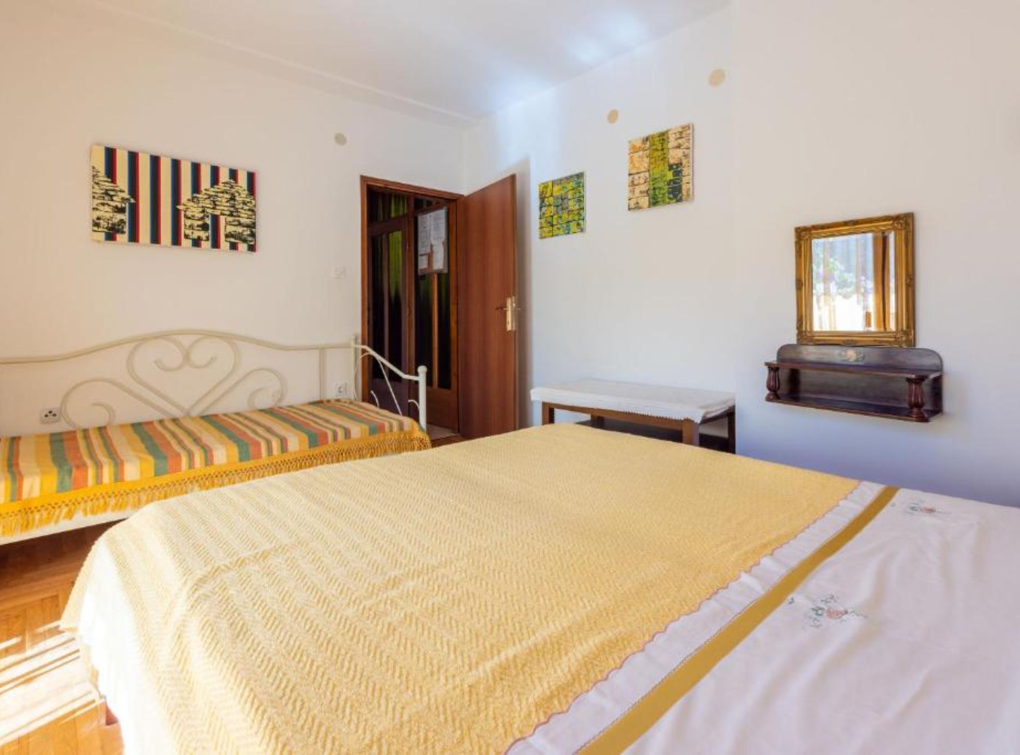 A bedroom with two beds, a wooden door, a small table, and wall art.