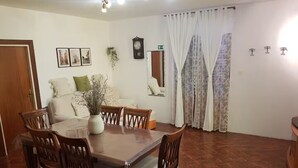 A dining area with a wooden table and chairs, a vase with flowers, a clock on the wall, and a window with curtains. - Villa Solea (Hvar)