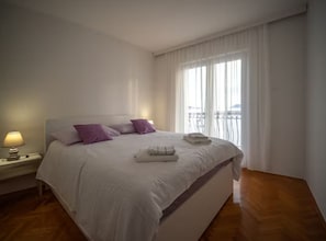 Een hotelkamer met een groot bed, een nachtkastje met een lamp, en uitzicht door het raam.