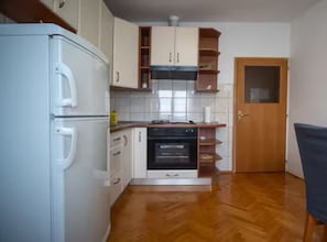 Een kleine keuken met een koelkast, oven en houten keukenkastjes.