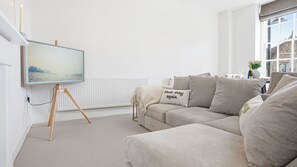 Una sala de estar moderna con un sofá beige, un cuadro en la pared y una ventana con vistas a un edificio.