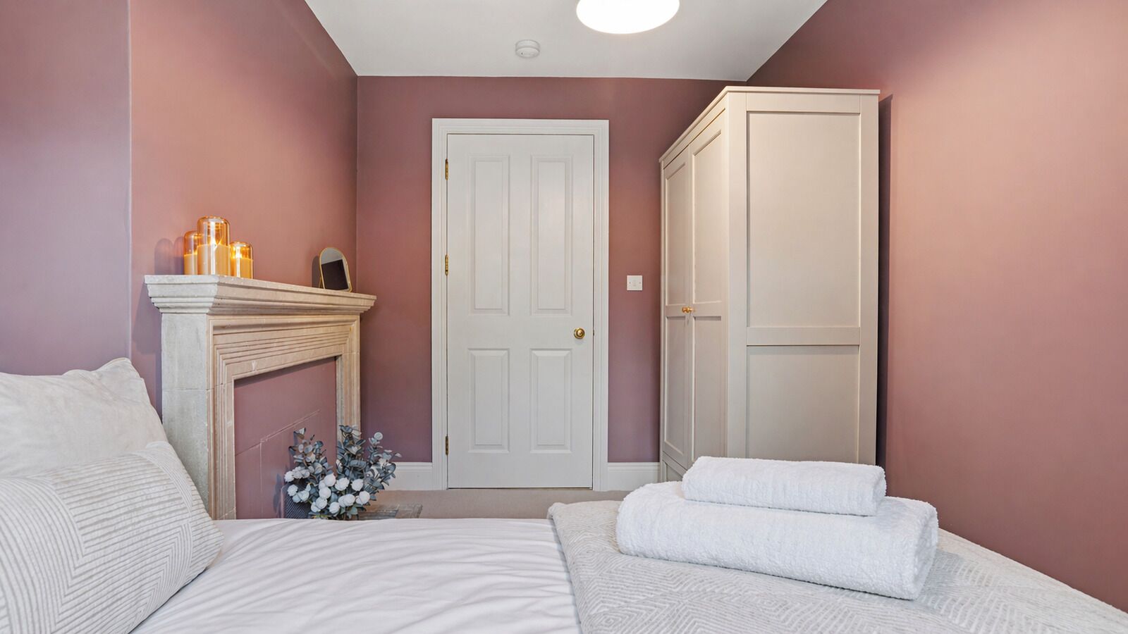 Um quarto com uma cama, um guarda-roupa branco, uma lareira e uma porta.