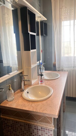 Ein Badezimmer mit zwei Waschbecken, einem Spiegel, einer Seifenspender und einem Fenster mit Vorhängen.