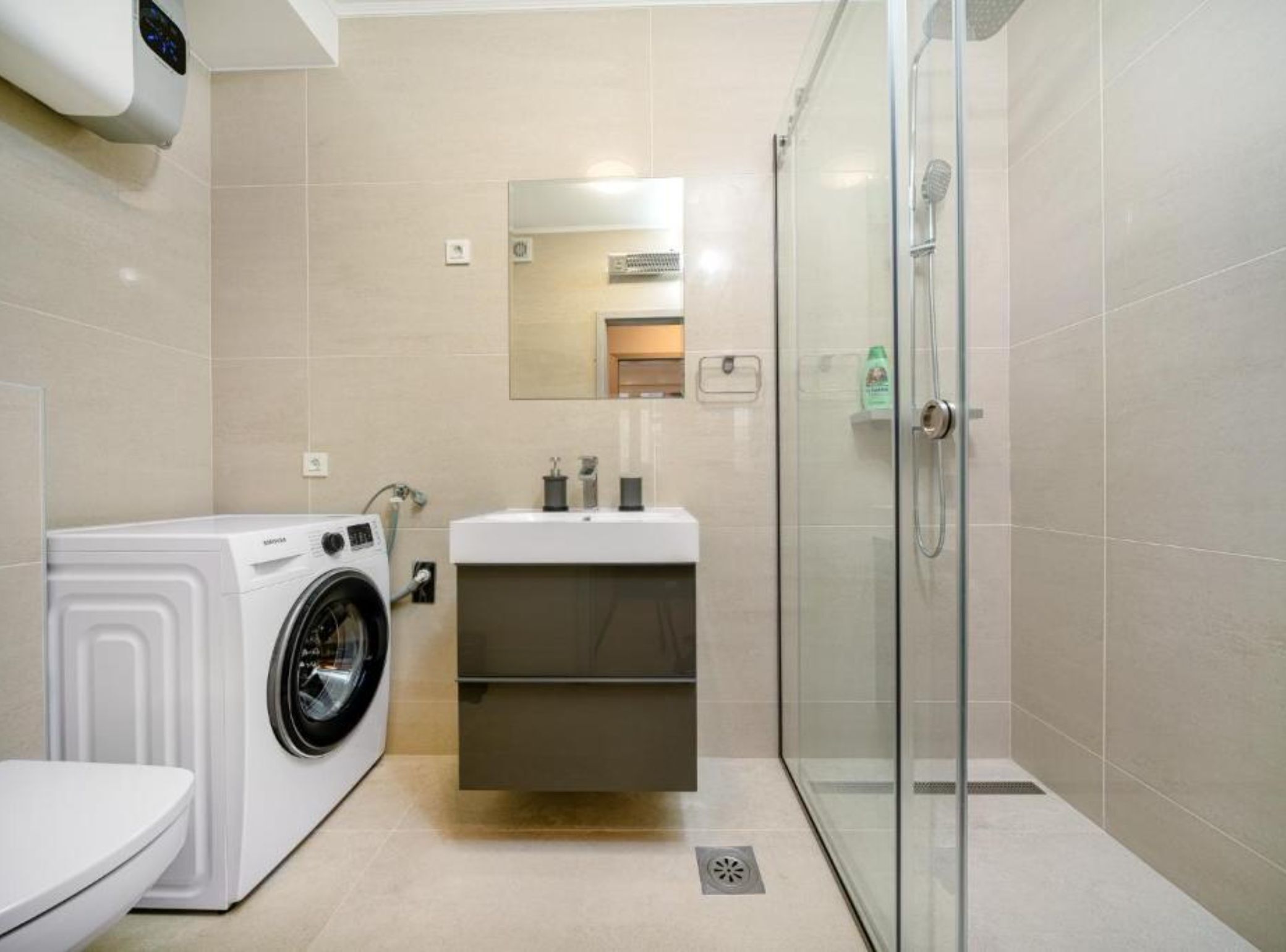 A bathroom with a washing machine, a sink, a mirror, and a glass shower enclosure.