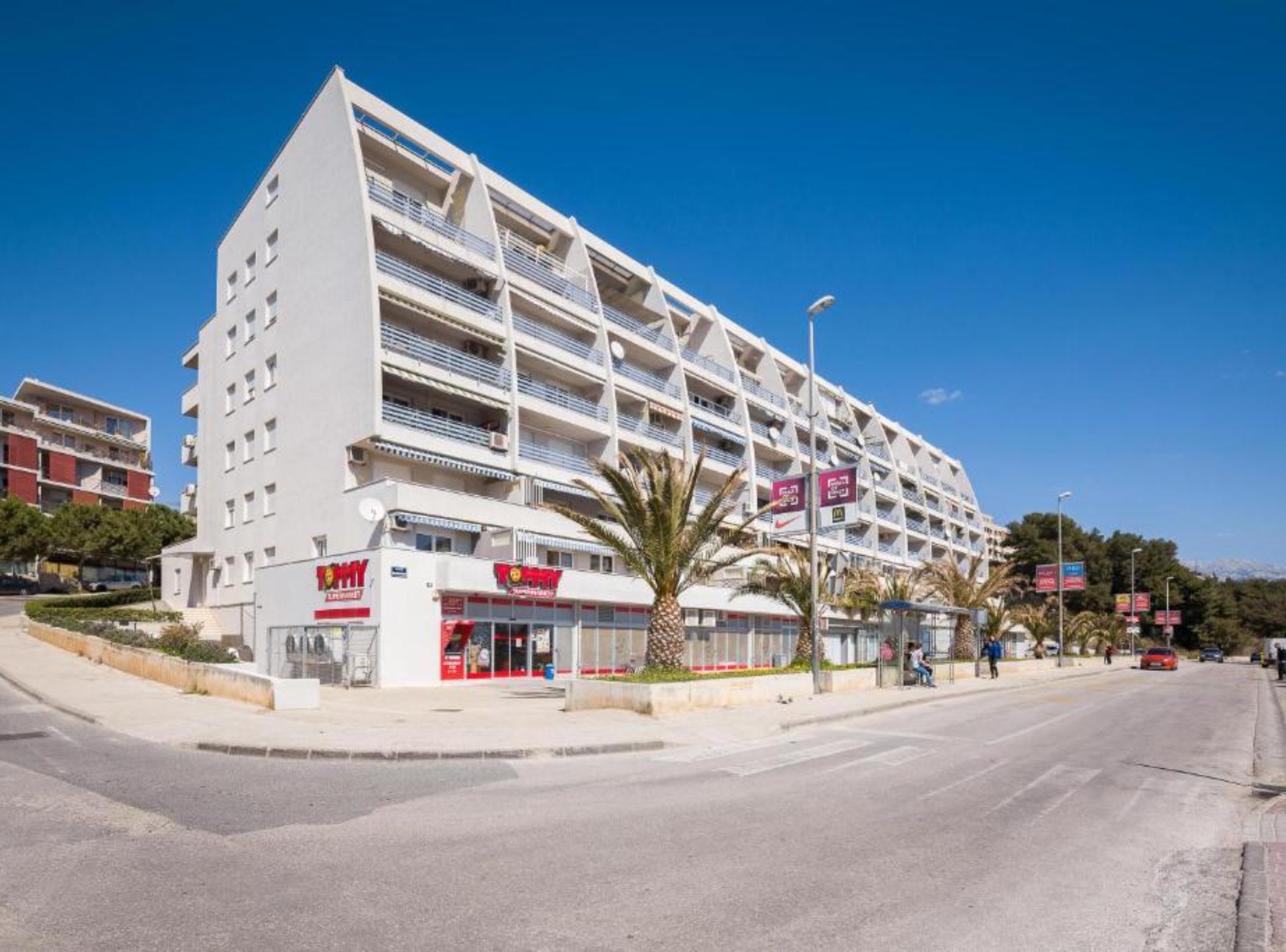A multi-story hotel with balconies, a ground-level restaurant, and a clear blue sky.
