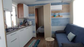 A compact kitchen with a gas stove, white cabinets, and a blue-striped wall. A small round table and a blue sofa with a cushion are in the living area.