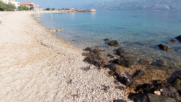 A pebble beach with clear water, rocky shoreline, and distant mountains. - Azzuro Sea Retreat Mobile Home (Razanac)