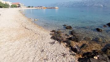 A pebble beach with clear water, rocky shoreline, and distant mountains.