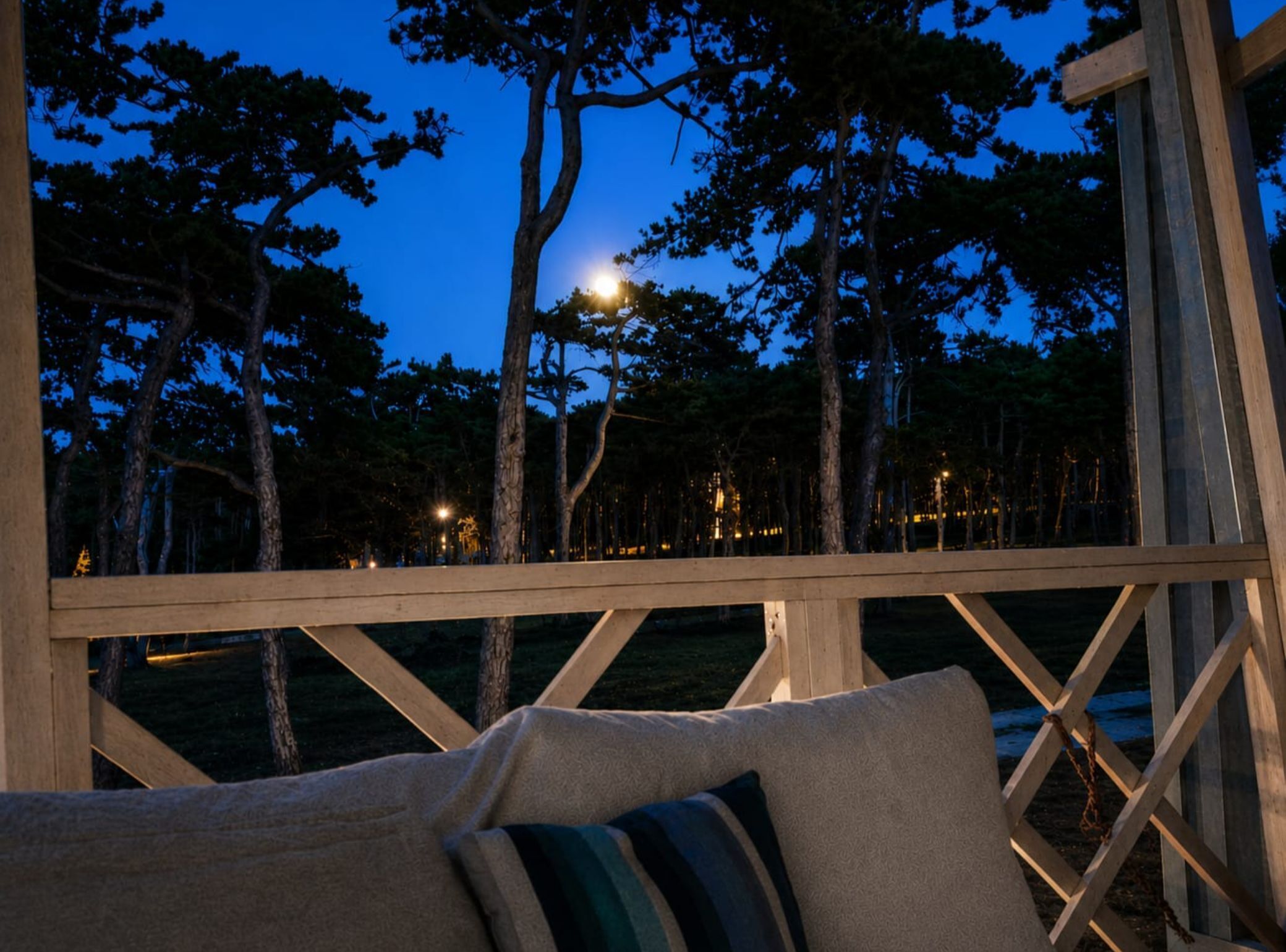 A wooden deck with a view of trees and a distant light source.