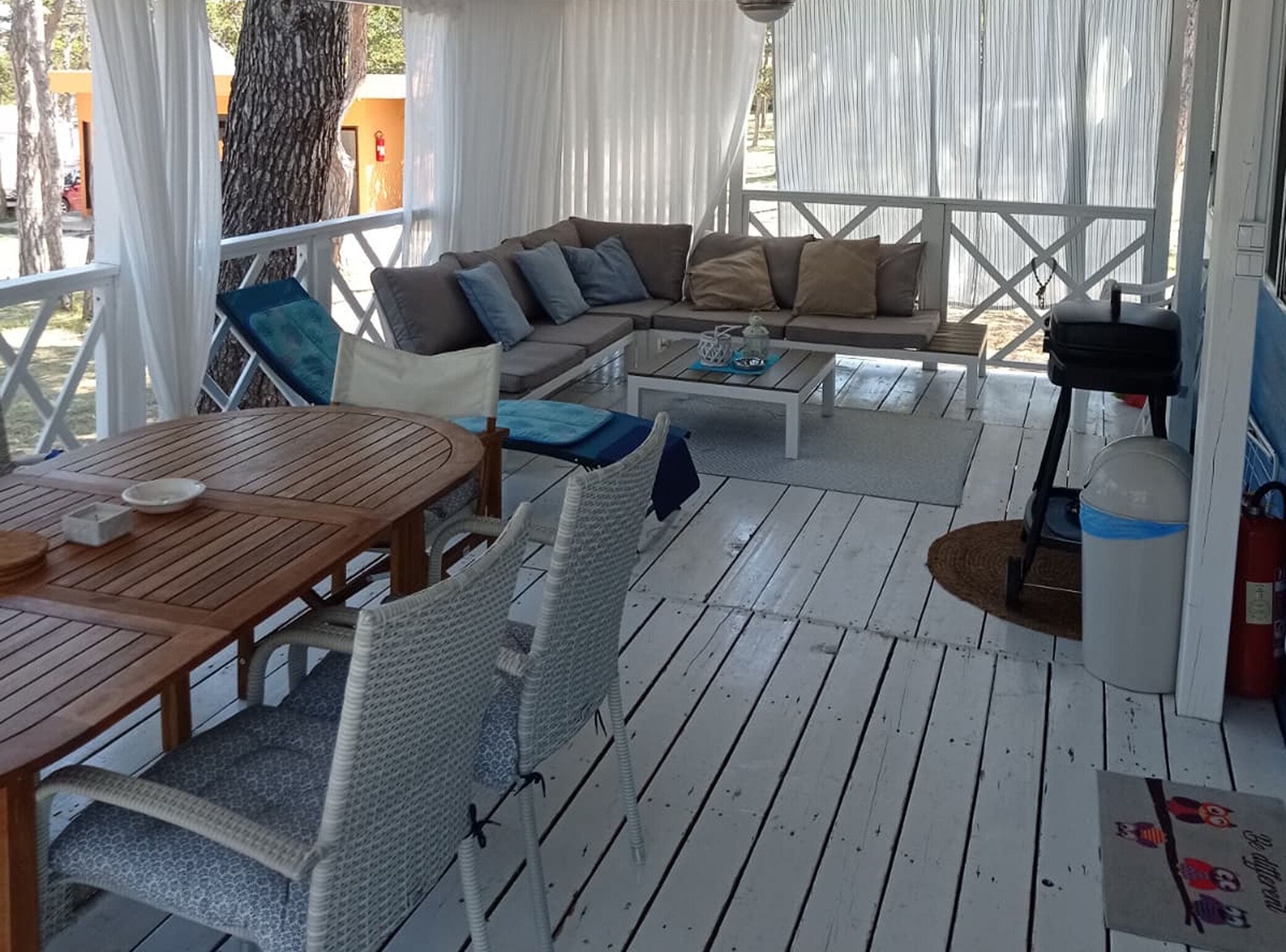 A covered outdoor seating area with a wooden table, wicker chairs, a sofa with cushions, and a small table with a candle.